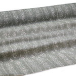 Draped fabric coming off a roll with monochomatic geometric stripe and mottled textural background in shades of grey.