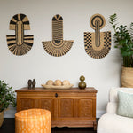 Living room scene with three black and tan sculptural woven panels, ornately carved wooden chest, baskets with house plans, white upholstered side chair and a stripe patterned footstool in orange.