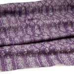 Draped fabric coming off a roll with monochomatic geometric stripe and mottled textural background in shades of purple.