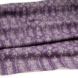 Draped fabric coming off a roll with monochomatic geometric stripe and mottled textural background in shades of purple.