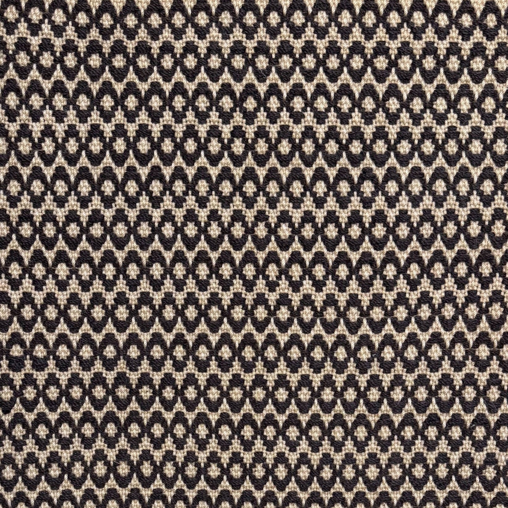 Handwoven wool rug with textural oval pattern in dark brown on a beige field. 