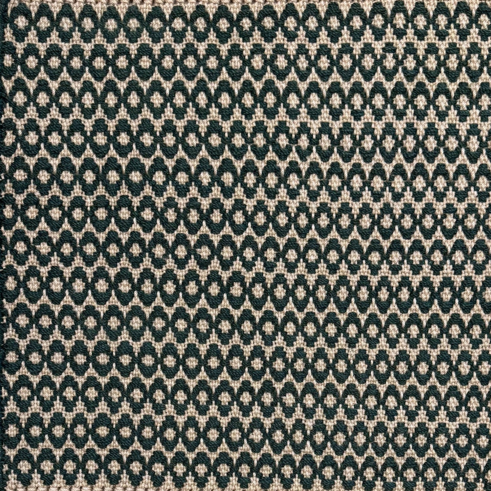 Handwoven wool rug with textural oval pattern in dark green on a beige field. 