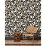 A wooden chair and end table in front of a wall papered in a painterly geometric pattern in shades of blue, cream and olive.