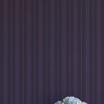 Vase of flowers on a white surface with a dark purple striped wallpaper background