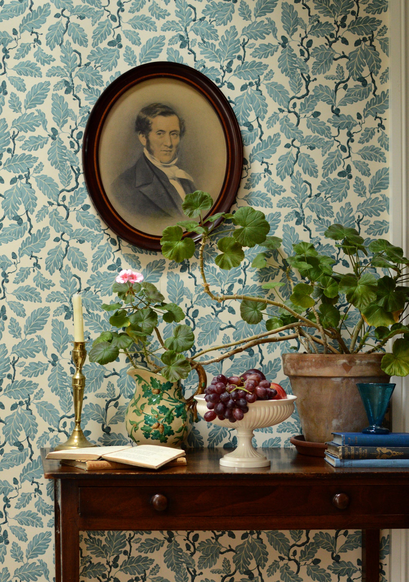 Decorative room interior with floral wallpaper, a portrait, and plants on a wooden table.