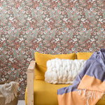 A couch covered in a throw pillow and blanket stands in front of a wall papered in a dense floral print in green and pink.