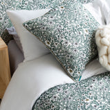 A bed with a headboard, duvet and pillows upholstered in a dense floral print in white, tan and green on a white field.