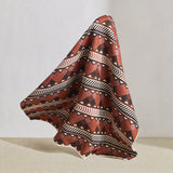 Hanging fabric in a complex stripe with geometric shapes and chevrons in clay, lilac, brown and cream.