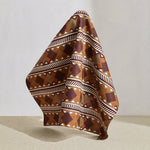 Hanging fabric in a complex stripe with geometric shapes and chevrons in taupe, orange, oxblood and cream.