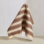Hanging fabric in a complex geometric stripe in maroon, ochre, ecru and black on a cream field.