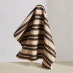 Hanging fabric in complex geometric stripe in brown, tan, orange, light purple and black on a cream field.
