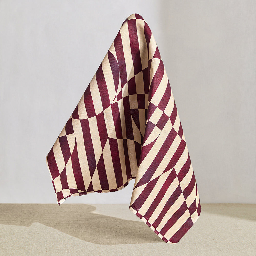 Draped fabric in a trompe l'oeil stripe pattern with geometric shapes in cream and burgundy. 