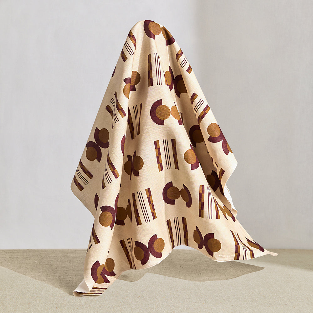 Hanging fabric in a graphic geometric pattern of circles and stripes in maroon and ochre on a cream field. 