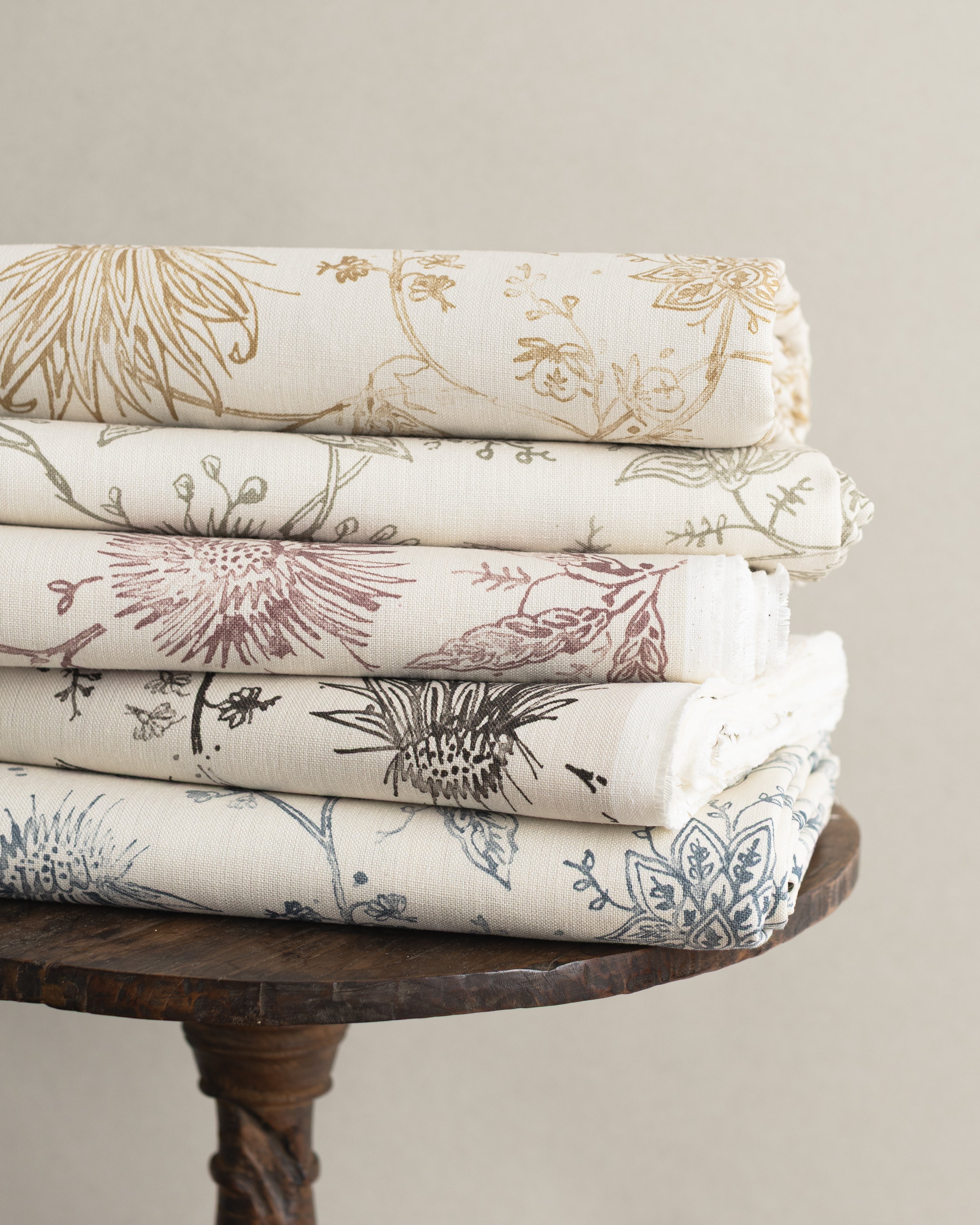 Wooden side table with stacks of folded fabric in floral design in various colors. 