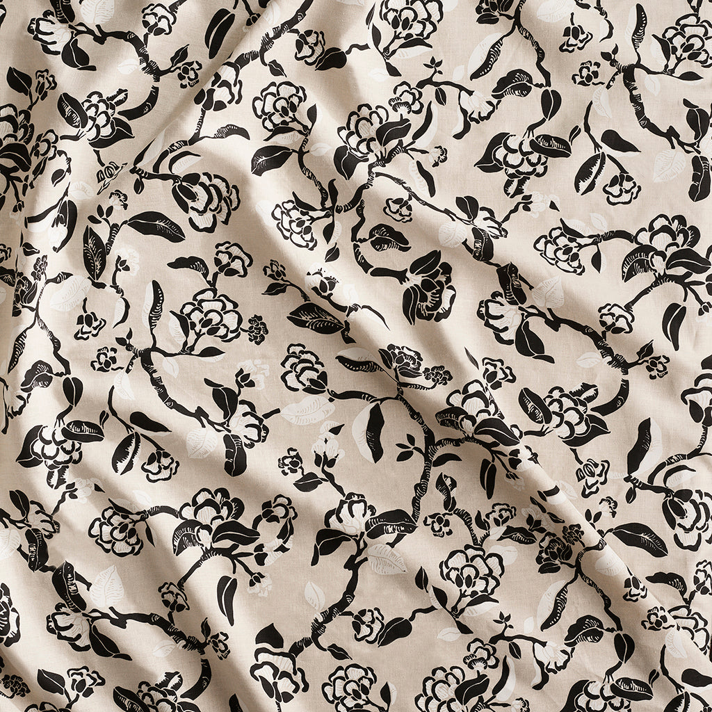 Close up of gently draped printed linen in a hand drawn branch and flower design in black and white on beige. 
