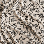 Close up of gently draped printed linen in a hand drawn branch and flower design in black and white on beige. 