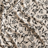 Close up of gently draped printed linen in a hand drawn branch and flower design in black and white on beige. 