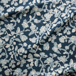 Close up of gently draped printed linen in a hand drawn branch and flower design in light blue and white on navy blue.