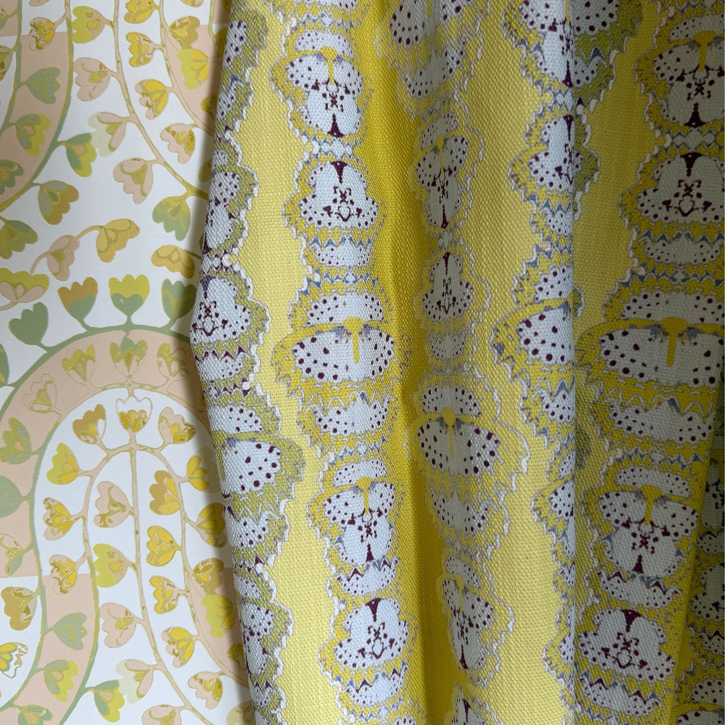 Draped fabric in yellow butterfly stripe against yellow floral wallpaper. 