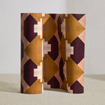 Wallpaper roll in a bold abstract checkerboard pattern in blush, oxblood, camel and cream.