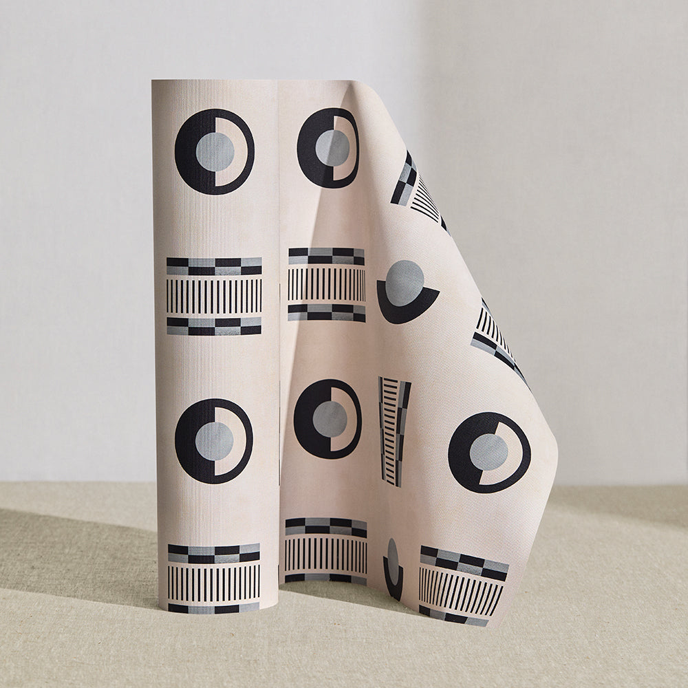 Wallpaper roll in a graphic geometric pattern of circles, and stripes in black and grey on a cream field.