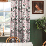 A cozy dining room with a large window and curtains in a minimalist floral grid print in white and green on a pink field.