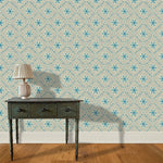 A wooden end table and lamp stand in front of a wall papered in an intricate floral lattice print in blue and tan.