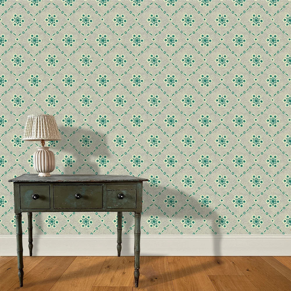 A wooden end table and lamp stand in front of a wall papered in an intricate floral lattice print in green, gray and cream.