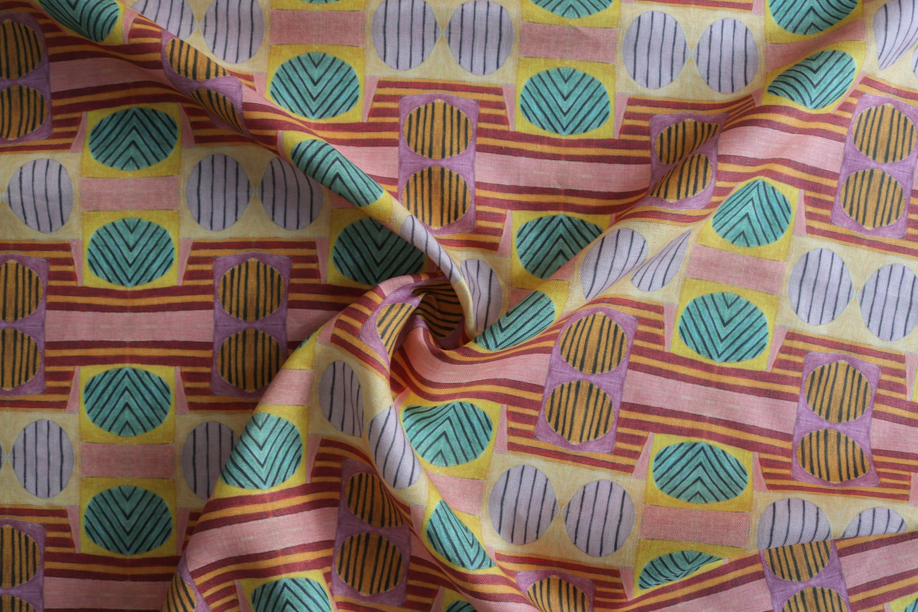 Close up of gently draped printed fabric with a complex geometric and striped pattern with pink, orange, turquoise and red. 