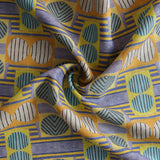 Close up of gently draped printed fabric with a complex geometric and striped pattern with yellow, blue, orange and pale pink. 