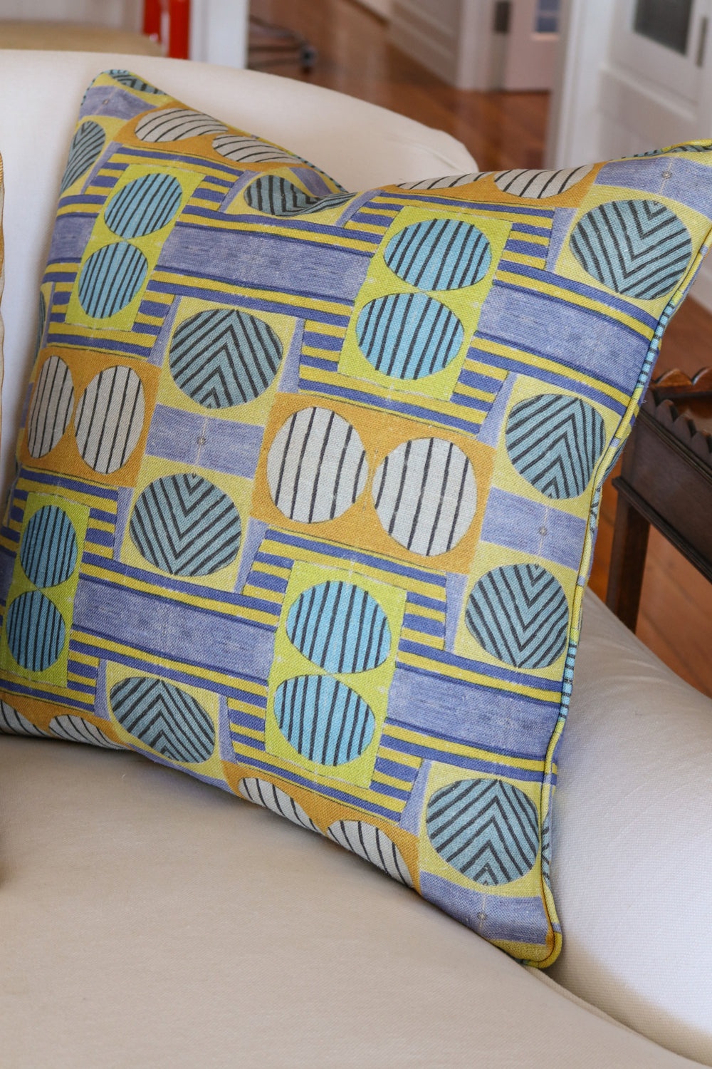 Close up of white couch with a bold geometric patterned pillow in yellow, orange and blue.
