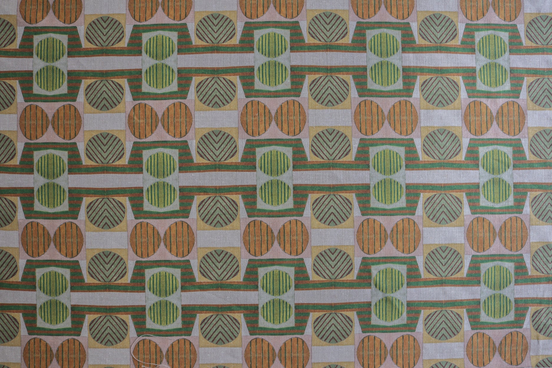 Close up of printed fabric with a complex geometric and striped pattern with orange, brown, grey and green.