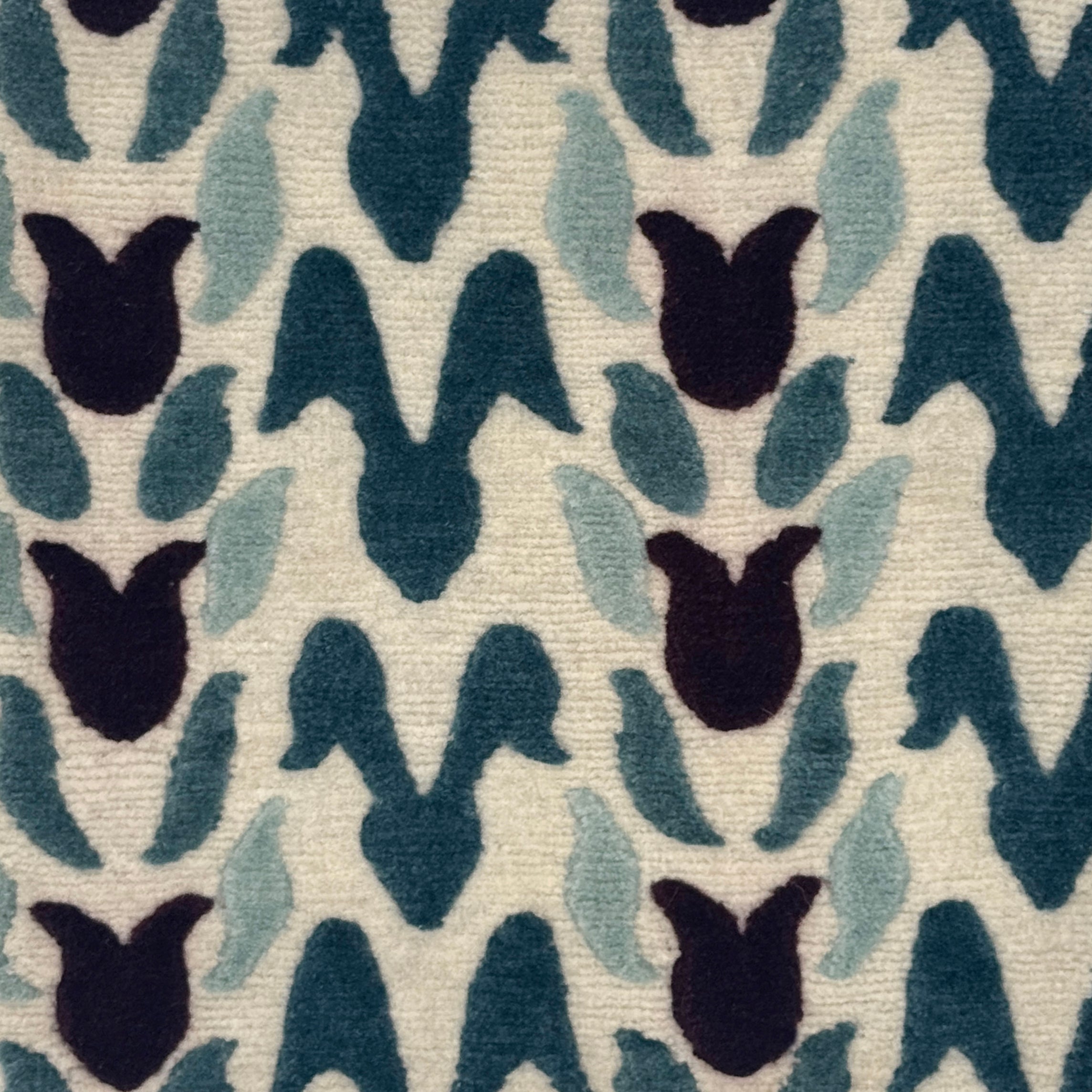 A close-up of a handknotted rug with an abstract petal design in wine purple, teal and aqua blue on a cream field. 