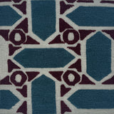 A close-up of a handwoven rug featuring geometric shapes in slate blue, deep plum, and off-white.