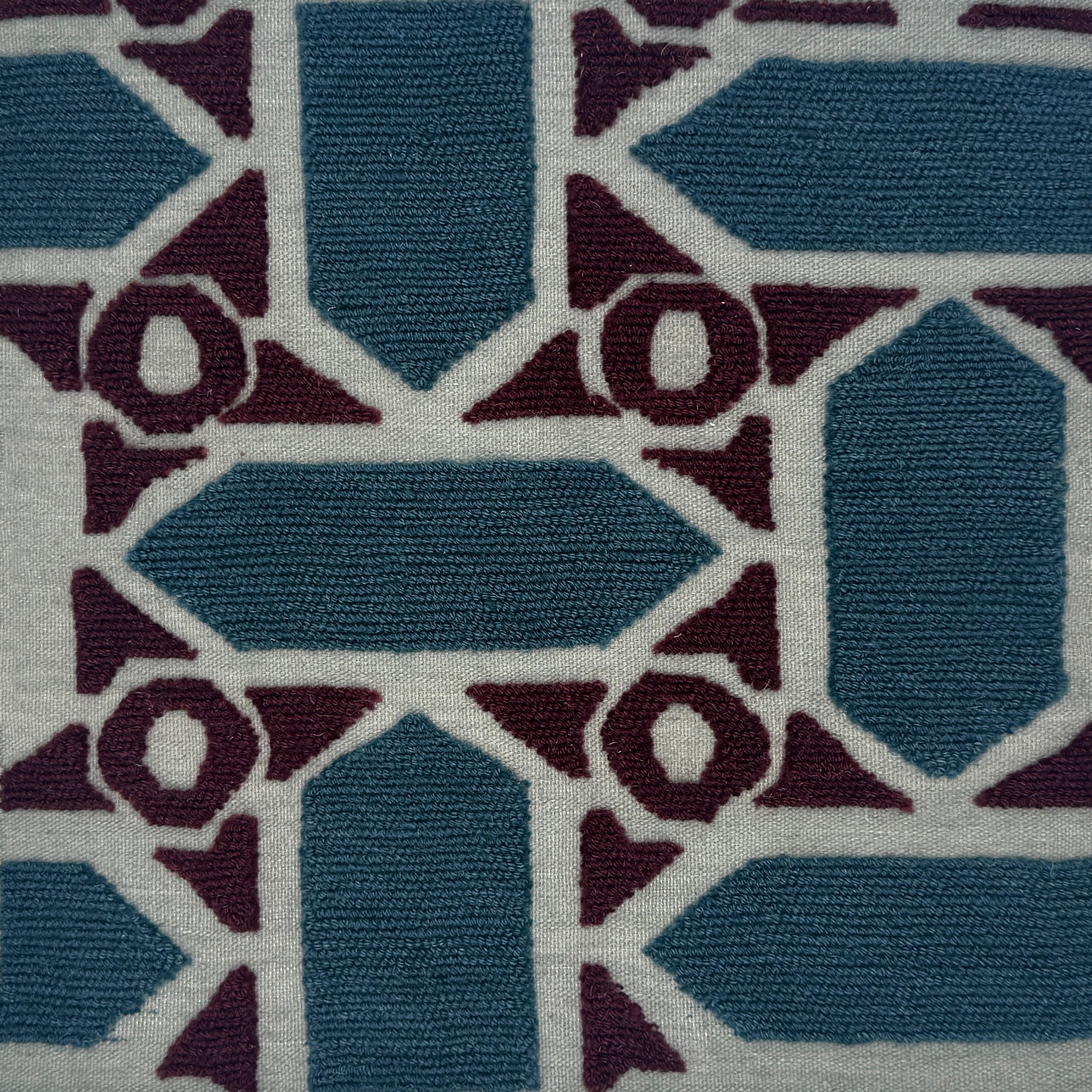 A close-up of a handwoven rug featuring geometric shapes in slate blue, deep plum, and off-white.
