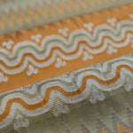 Close-up of patterned fabric with wavy lines and geometric shapes in orange, ivory and green. 