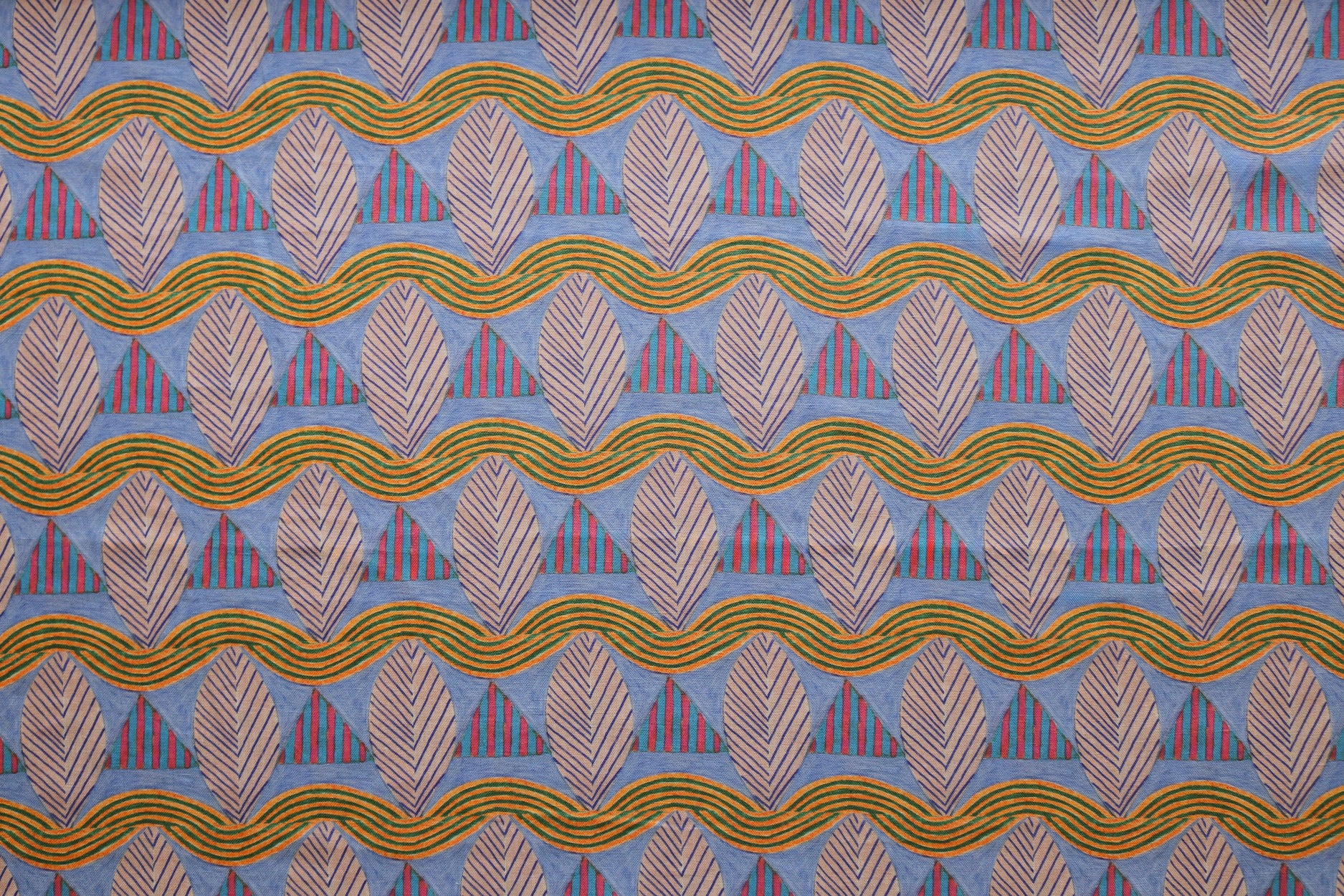 A close-up of a patterned fabric featuring repeating rows of stylized pink leaves, blue and red striped triangles and wavy orange-green lines on a blue background