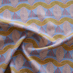 A close-up of a gently draped patterned fabric featuring repeating rows of stylized pink leaves, blue and red striped triangles and wavy orange-green lines on a blue background
