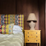 A cozy bedroom tableau with a headboard and throw pillows upholstered in a playful geometric stripe print.