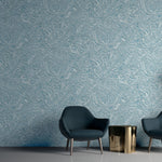 Two navy lounge chairs in front of a wall papered in a painterly botanical print in white and blue on a light blue field.