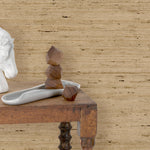 End table with marble and wood scupltures in front of a wall papered in textured tan arrowroot grasscloth.