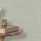 End table with books and  vintage phone in front of a grasscloth wallpaper with a herringbone weave in cream and aqua.
