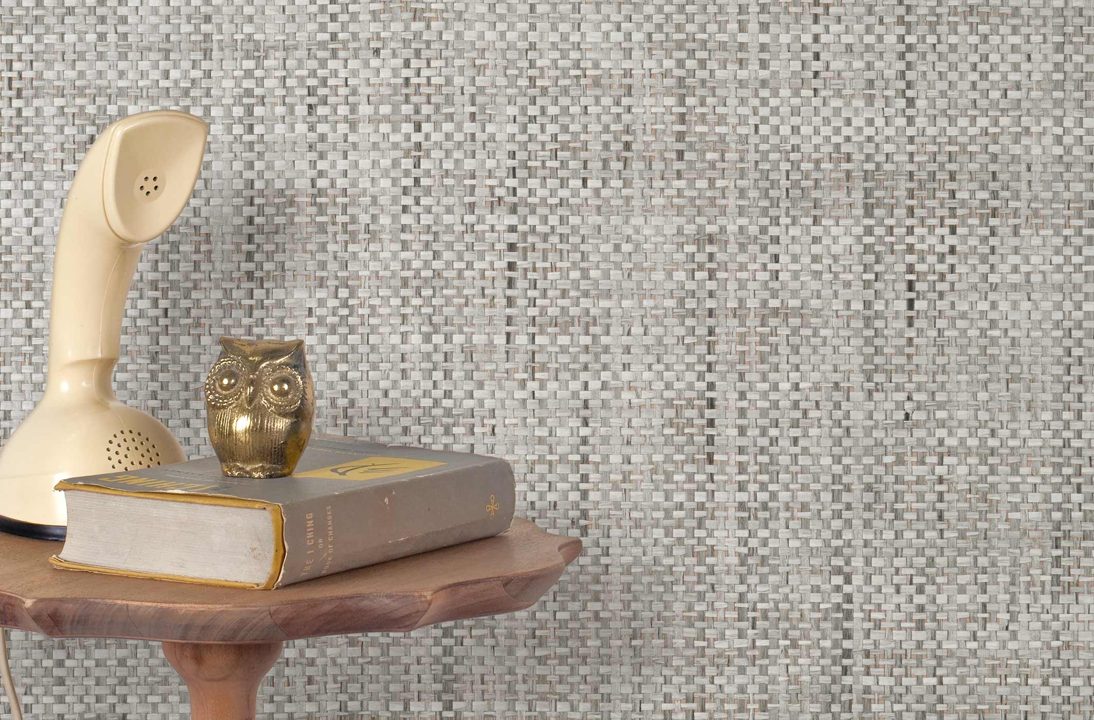 End table with a phone, book and owl sculpture in front of a wall covered in paperweave grasscloth in mottled gray.