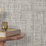 End table with a phone, book and owl sculpture in front of a wall covered in paperweave grasscloth in mottled gray.