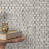 End table with a phone, book and owl sculpture in front of a wall covered in paperweave grasscloth in mottled gray.