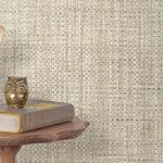 End table with a phone, book and owl sculpture in front of a wall covered in paperweave grasscloth in mottled cream and gray.
