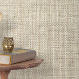 End table with a phone, book and owl sculpture in front of a wall covered in paperweave grasscloth in mottled cream and gray.