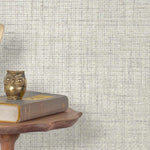 End table with a phone, book and owl sculpture in front of a wall covered in paperweave grasscloth in metallic cream and gray.
