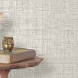 End table with a phone, book and owl sculpture in front of a wall covered in paperweave grasscloth in metallic cream and gray.