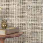 End table with a phone, book and owl sculpture in front of a wall covered in paperweave grasscloth in mottled cream and black.